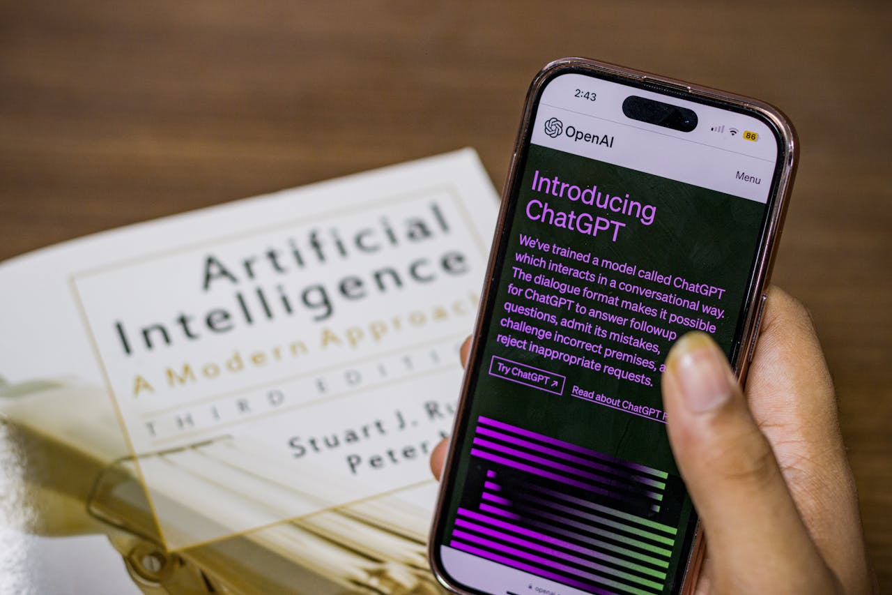 about-us Close-up of a smartphone displaying ChatGPT app held over AI textbook.
